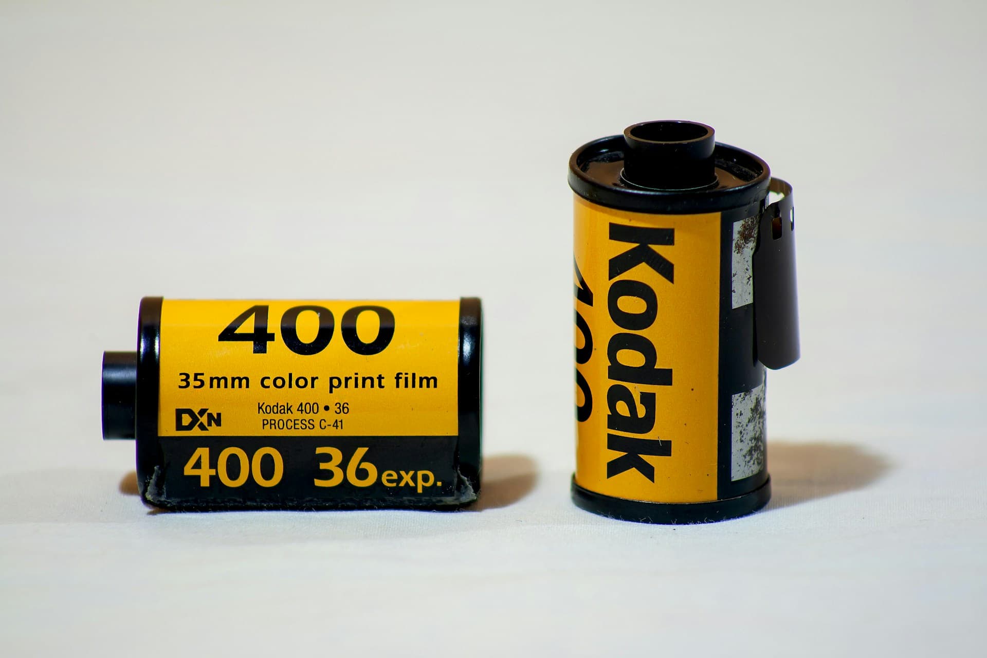 Two rolls of Kodak 35mm film rest next to a film camera on a wood surface