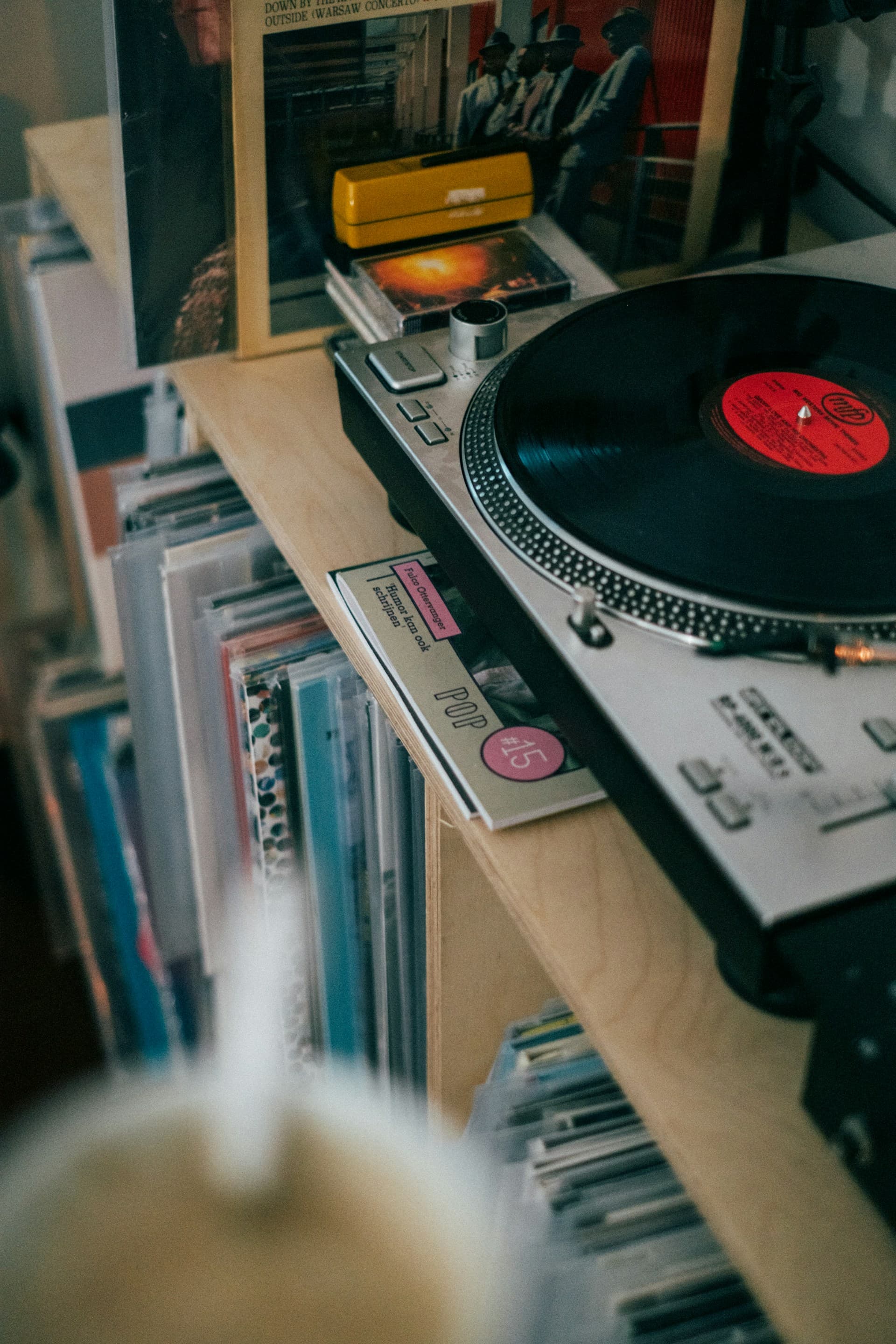 A modern turntable sits on a wooden shelf in a quiet room
